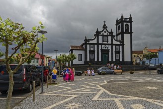 Square with historic church Nossa Senhora da Luz in the background, people in traditional dress,