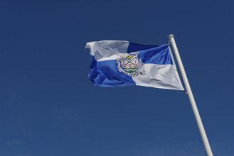 Close-up of a blue and white flag of the Capalas region in the wind on a flagpole against a bright