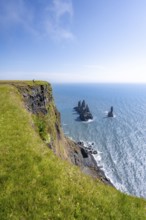 Young man standing on cliff, view from steep cliff to the rocks Reynisdrangar in the water, at