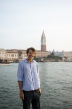 Young man in striped shirt and shorts on the banks of the Grand Canal, behind Campanile, Venice,