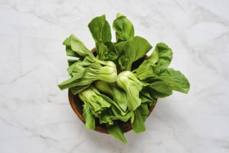 Vibrant green bok choy is neatly arranged in a rustic wooden bowl, set against a clean marble