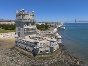 A tower on a riverbank with a bridge in the background and a clear blue sky, aerial view, Torre de