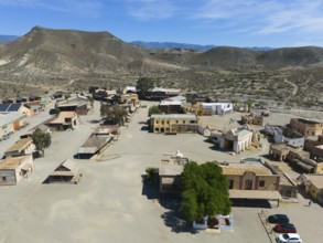 A western town with scattered trees and historic buildings in a dry, mountainous landscape, aerial