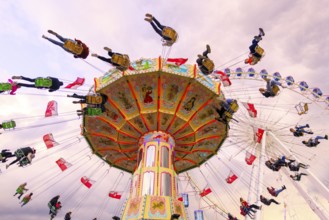 Chain carousel in motion with cheerful people in front of a cloudy sky, Ferris wheel, wave flight,