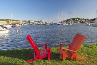 Two red wooden chairs on a lawn overlooking a sunny harbour, Sandefjord, Norway, Europe