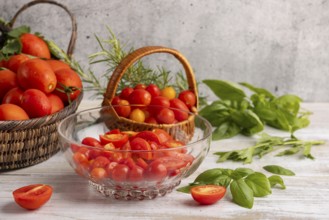 Sliced tomatoes in a glass bowl, surrounded by fresh tomatoes in baskets, basil and rosemary