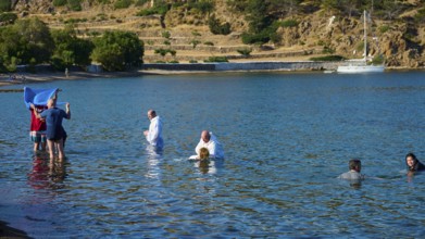 Men in white clothes and swimming costumes in the water during a traditional ceremony in a hilly