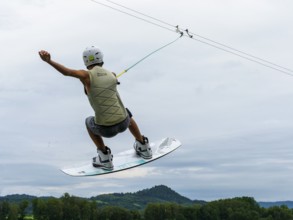 Young man jumping with wakeboard over the lake, water sports, water skiing in wakepark, Stráž pod