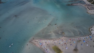 Overtourism, aerial view of a beach with many people and colourful umbrellas, surrounded by