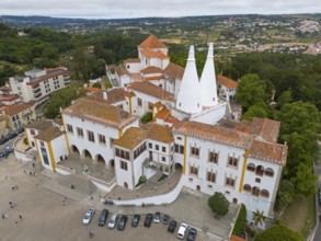 Aerial view of a large historic palace with distinctive double-cone towers and orange-red roofs,