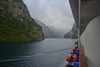 A cruise ship, my ship 6, sails through a misty fjord surrounded by green mountains and waterfalls,