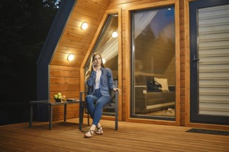 Late at night a girl sits on the terrace of a tiny house and talks on the smartphone with her