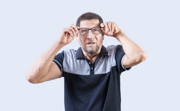 Surprised senior man taking off glasses looking at camera. Amazed senior man taking off glasses