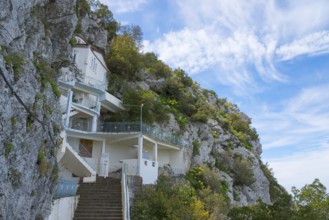 White building on a hillside with a stone staircase and surrounded by nature, rock church of