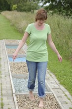 Woman walking barefoot over glass gravel and bottle corks, barefoot path Tilbeck Abbey, Havixbeck,