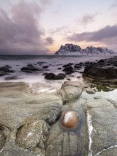 Rounded rocks on Utakleiv beach in a dramatic cloudy atmosphere, snow-capped mountains in the