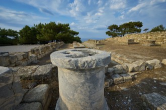 Stone column in the middle of an ancient ruins field with trees and stone structures in the