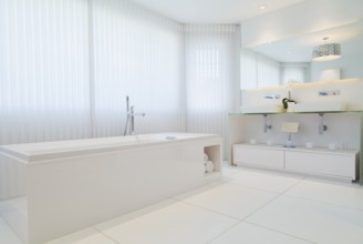 White elongated rectangular bathtub and cabinets with large wall mirror in en suite with ceramic