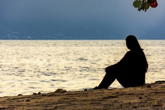 Girl sitting in front of the sea during sunset in Ilhabela on the north coast of São Paulo, Sao