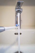 A bathroom tap is running while a toothbrush is held under the running water, symbolic image of