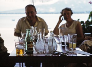 Menschen um einen Tisch mit Getränken und Flaschen in einem Hafencafé in Calvi, Korsika,