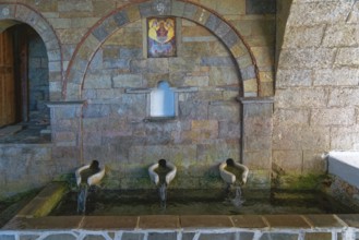 Ancient stone fountain with three water sources, marble basin and mural below the Panagía church,