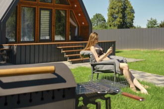 Serene woman enjoying a peaceful moment on a sun lounger in the backyard of a modern A-frame house