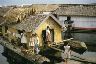 Woman and children in an informal housing area with wooden huts built on logs, known as the