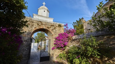 Old wall arch with a view of a church surrounded by flowering plants, Koroni, Byzantine fortress,