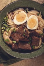 Asian noodles in broth, with beef and egg, top view, close-up, no people