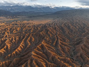 Landscape of eroded hills, badlands at sunset, mountain peaks of the Tian Shan Mountains in the