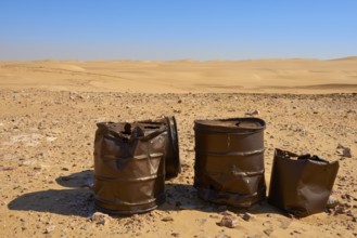 Rusty barrels stand in a vast, sandy desert landscape under a clear blue sky, Matruh, Great Sand