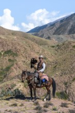 Traditional Kyrgyz eagle hunter with eagle in the mountains, hunting on horseback in front of dry