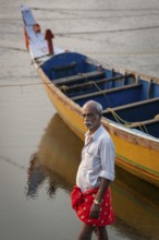 Fisherman with red dhoti in front of yellow-blue painted fishing boat, Fort Cochin, Kochi, Kerala,