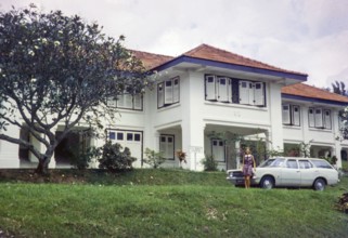 Woman in front of large colonial mansion building originally used by British army, standing by Ford