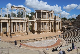 Roman theatre with monumentally preserved façade and rows of seats, people visit the ruins under a