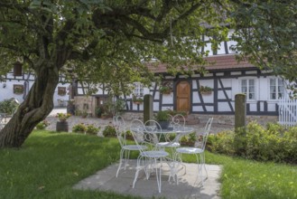 Idyllic garden with white iron furniture and half-timbered house in the background, Hunspach,