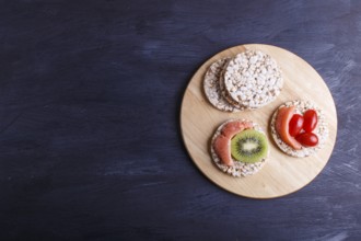 Rice cakes with salmon, kiwi and cherry tomatoes on dark wooden background. top view, copy space