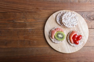 Rice cakes with salmon, kiwi and cherry tomatoes on wooden background. top view, copy space