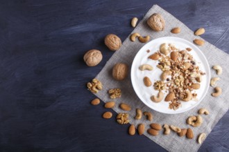 White plate with greek yogurt, granola, almond, cashew, walnuts on black wooden background. top