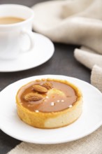 Sweet tartlets with almonds and caramel cream with cup of coffee on a black concrete background and