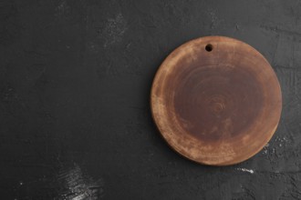 Empty round wooden cutting board on black concrete background. Top view, copy space, flat lay