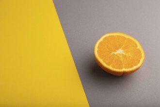 Ripe cut orange on gray and yellow pastel background. Side view, copy space. Tropical, healthy