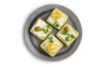 Green cracker sandwiches with cream cheese and cherry tomatoes on gray plate isolated on white