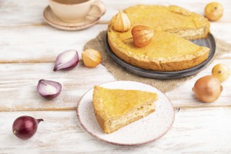 Autumn onion pie and cup of coffee on white wooden background and linen textile. Side view, close