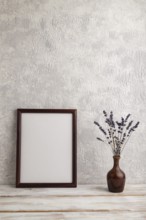 Brown wooden frame mockup with lavender in ceramic vase on gray concrete background. Blank,