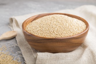 Wooden bowl with raw white quinoa seeds and wooden spoon on a gray concrete background and linen