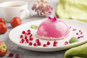 Pink mousse cake with strawberry and a cup of coffee on a gray concrete background and green