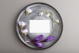 White paper invitation card, mockup with crocus and galanthus flowers on ceramic plate and gray