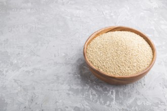 Wooden bowl with raw white quinoa seeds on a gray concrete background. Side view, close up, copy